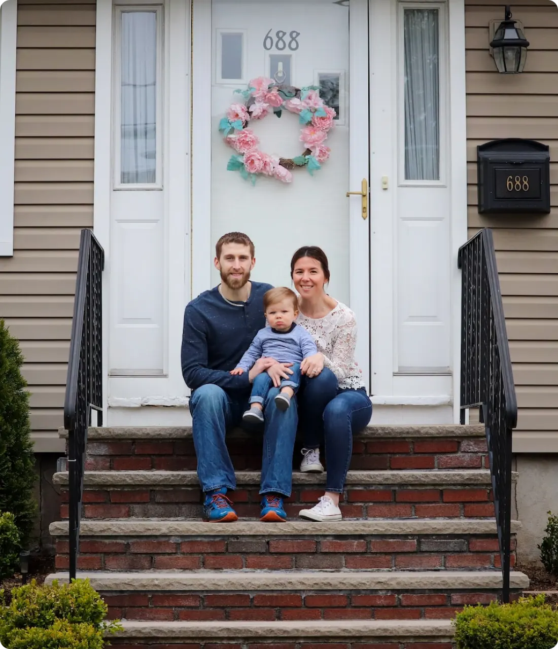 section1-image-webp An image of a couple with their son sitting on a stair in front the main door of their house.